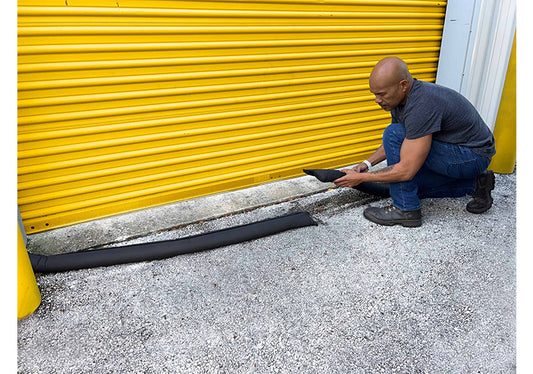 A black sand-less sandbag barrier activated by water, placed against a door to prevent flood waters from entering a property.
